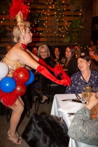Burlesque performer adorned with red feathers and a balloon skirt entertaining guests at a French-themed dinner night in Sydney