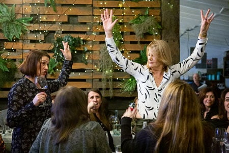 Woman raising arms in celebration at Cup and Cook's French Dinner Night.