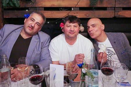 Three men with decorative flowers in their hair smiling at Cup and Cook's French Dinner Night in Sydney